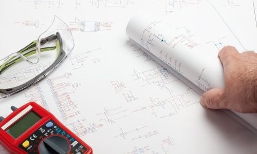 Engineer reviewing schematics with multimeter and safety glasses Engineer reviewing schematics with multimeter and safety glasses